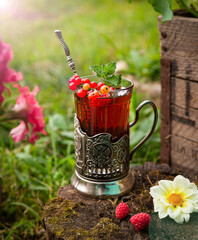 tea with berries in a glass cup against the backdrop of a summer sunny garden. summer still life with tea. concept summer, garden, relaxation, tea drinking, herbal tea, tea with berries
