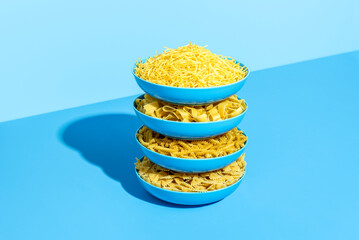 Raw pasta variety on a blue table. Stack of plates with uncooked pasta