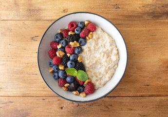 Bowl of oatmeal porridge with various berry and nuts on wooden table top view. Healthy and diet...