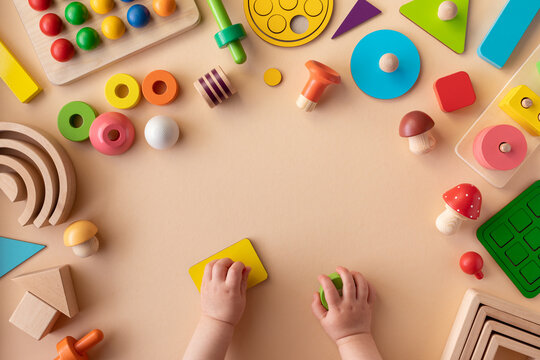 Toddler activity for motor and sensory development. Baby hands with colorful wooden toys on light table top view.