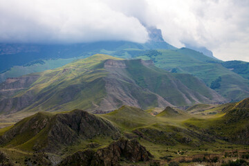 Dramatic landscape - steep cliffs and green hills with cloudy sky and fog on a summer day in the Elbrus region North Caucasus russia and soft blurred focus
