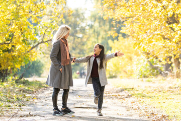 Little girl and her mother enjoy sunny weather in the autumn park