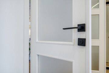 Fototapeta na wymiar Modern black door handle on white wooden door in interior. Knob close-up elements. Door handle, fittings for interior design