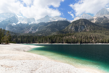 Panorama of the gentle shore of Tovel lake with emerald water and alpine mountain ranges covered...