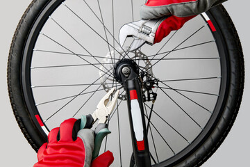 Hands in protective gloves with adjustable wrenches and pliers on the background of a bicycle wheel