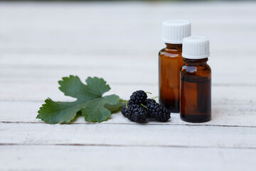 mulberry extract (oil, tincture, infusion, remedy) in glass bottle with fresh black mulberry fruit on white background