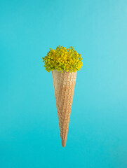 Ice cream cone with small yellow and green flowers on a light blue background.