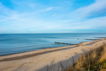 Fototapeta na wymiar Beautiful sandy coast of baltic sea with breakwaters, minor clouds and deep blue sky