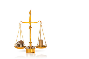 Small wooden house and stacked golden coins on weighing scales isolated on white background....