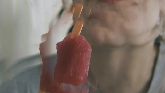 A girl laughs and eats a colorful popsicle, mouth and ice cream detail, filmed inside a house, in summer, in slow motion