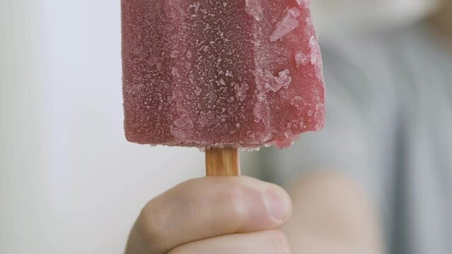 A hand brings a blueberry popsicle closer to the camera, detail and slow motion. You can see the details of the ice and the texture of the popsicle, it is very colorful and catchy