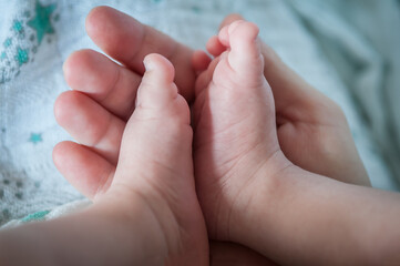 Close-up detail of parent holding cute and soft baby small leg in his hands. Macro abstract view of sweet baby foot fingers. Soft child skin feet. Love and family emotion