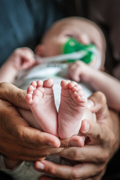 Close-up detail of parent holding cute and soft baby small leg in his hands. Macro abstract view of sweet baby foot fingers. Soft child skin feet. Love and family emotion
