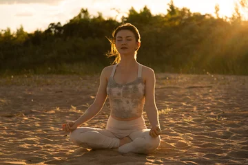 Foto auf Leinwand Woman practicing yoga outside in lotus pose on beach during sunset golden hour © Collab Media