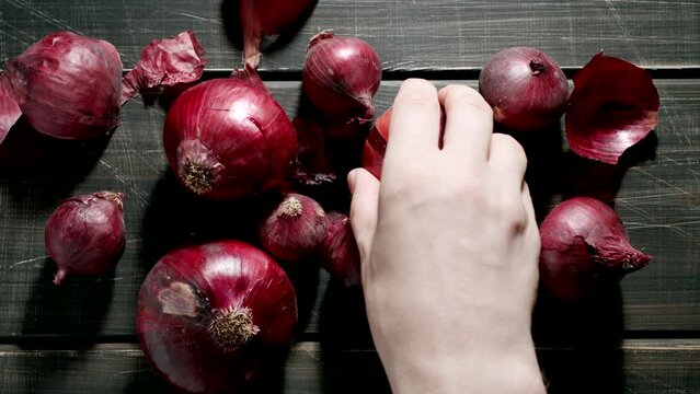 TOP VIEW: Human hand takes a red onion bulb on a wooden dark table