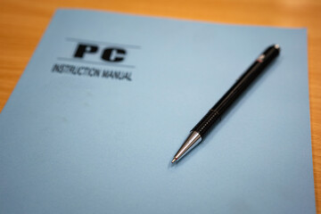 A ballpoint pen is placed on computer instruction manual's cover page. Object in working scene photo, selective focus.