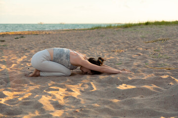 Woman practicing yoga outside in child's pose on beach