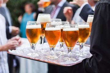 Waiter serving several beers in glasses on a tray to guests at an event, wedding, party, etc.