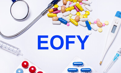 On a white background pills, stethoscope, syringe, thermometer and text EOFY. Medical concept
