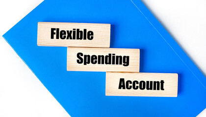 There is a blue notebook on a light gray background. Above are three wooden blocks with the words FSA Flexible Spending Account