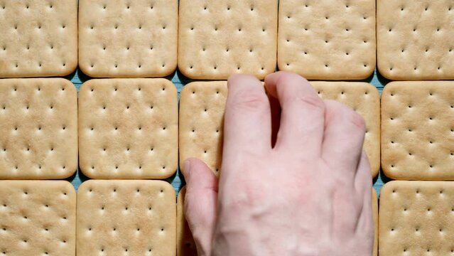 TOP VIEW: Human hand takes a cracker cookie from a blue table