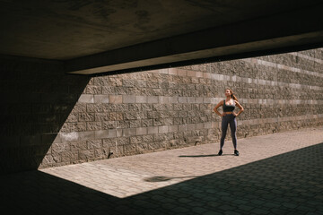 Beautiful young fit woman in sportswear catching her breath during run in the city. Copy space. Urban background.