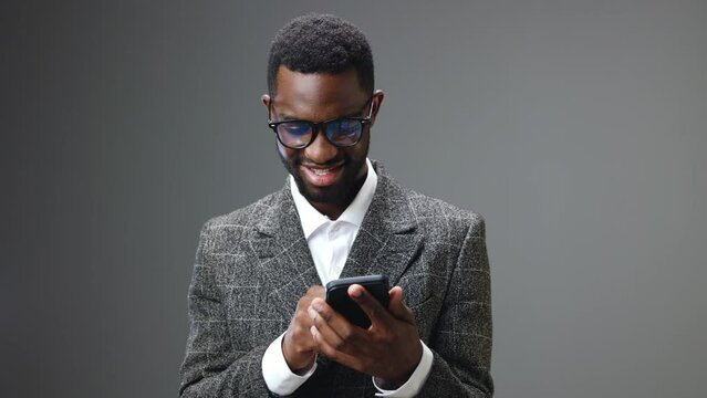 African american businessman man holding a phone looking at it and smiling while typing a message and browsing apps