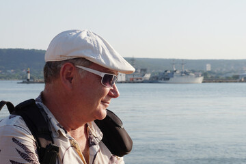 portrait of a smiling middle-aged man in sunglasses with a backpack on the sea