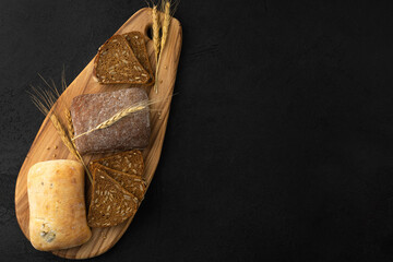 Different type of bread: gluten free, rye, wheat, on a wooden board on a black background