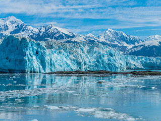 A view across icy water and islet towards the Hubbard Glacier in Alaska in summertime
