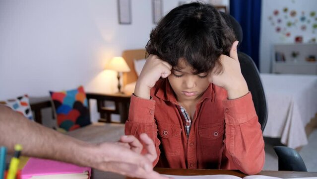 An Indian father is scolding his young boy for his studies - parental pressure  a stressed child  school homework. An Indian parent shouting at their son at home while he sits at a study table feel...
