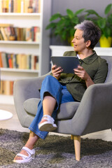 Mature woman using tablet computer while relaxing in chair and have conversation. Actual lifeshot...