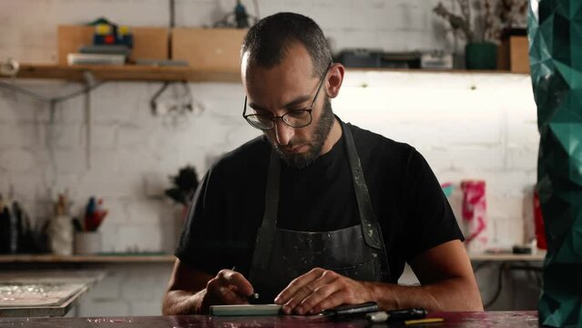 A man of Arab appearance sharpens a blade in a workshop. Sculptor, painter, needleworker.