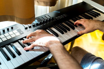 A close up of hands playing electric piano in home studio during the day