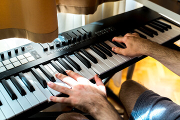 A close up of hands playing electric piano in home studio during the day