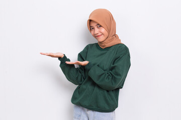Happy young asian muslim woman pointing with fingers to different directions isolated on white background
