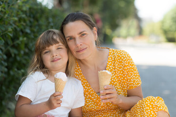 Mom and child daughter eat ice cream in the park on a summer day. happy family has fun together in...