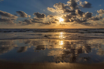 Obraz premium Sunset on the Mediterranean coast. Natural landscape. Mediterranean nature. Reflection, beautiful clouds, blue sky and yellow sunlight. Israel.