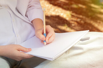Anonymous girl making notes in the blank paper album,sunlight on background.