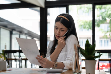 Business asian woman working with paperwork calculator at office while talking on phone,