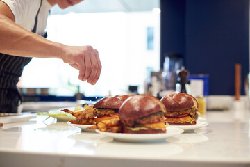 Close up chef hands sesoning oven fires potato with hot humburgers ina white plates. Fast food concept. Fresh and organic