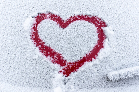 Snow red heart on the car window with copy space. Heart sign in fresh snowflakes. Heart shape symbol drawn on snowed car glass. Love concept. Valentine's Day. Declaration of love
