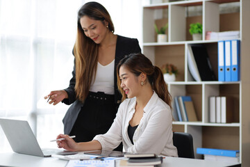 Fototapeta premium Attractive Asian businesswoman and secretary colleague discussing working on a business project at an office desk.