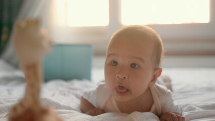 Happy baby lying on tummy on bed and looking at toy