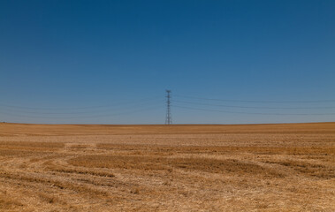 Transmission tower on wheat field against blue sky. Castilla y Leon, Spain