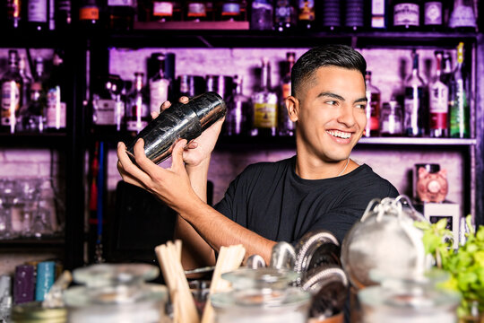 bartender with a shaker in his hands smile looking to the side at a nightclub bar