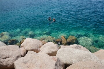 Silhouettes of divers in turquoise water next to a rocky shore in the Red Sea in Aqaba, Jordan