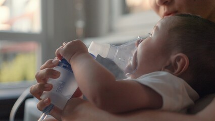 Side view of baby breathing an inhaler at home - obrazy, fototapety, plakaty