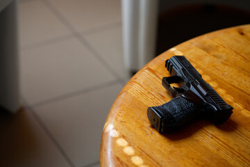black hand gun lays on a wooden table opened blurry doors shadows casted on the floor are in background. can be used ie for book cover