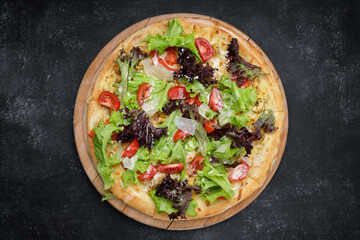 Pizza with chicken, mushrooms, lettuce and tomatoes on a wooden board, on dark concrete. top view
